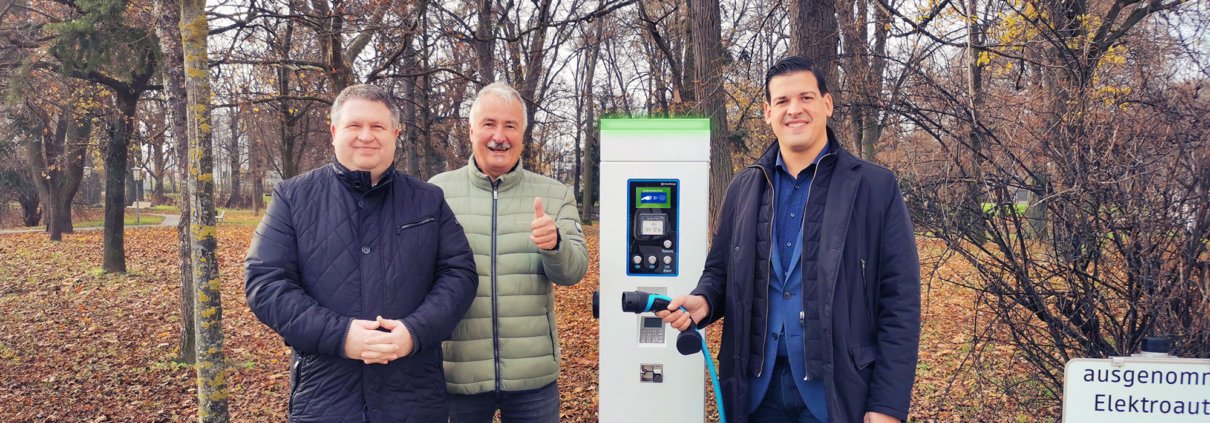 Drei personen stehen im Wald vor einer Ladesäule